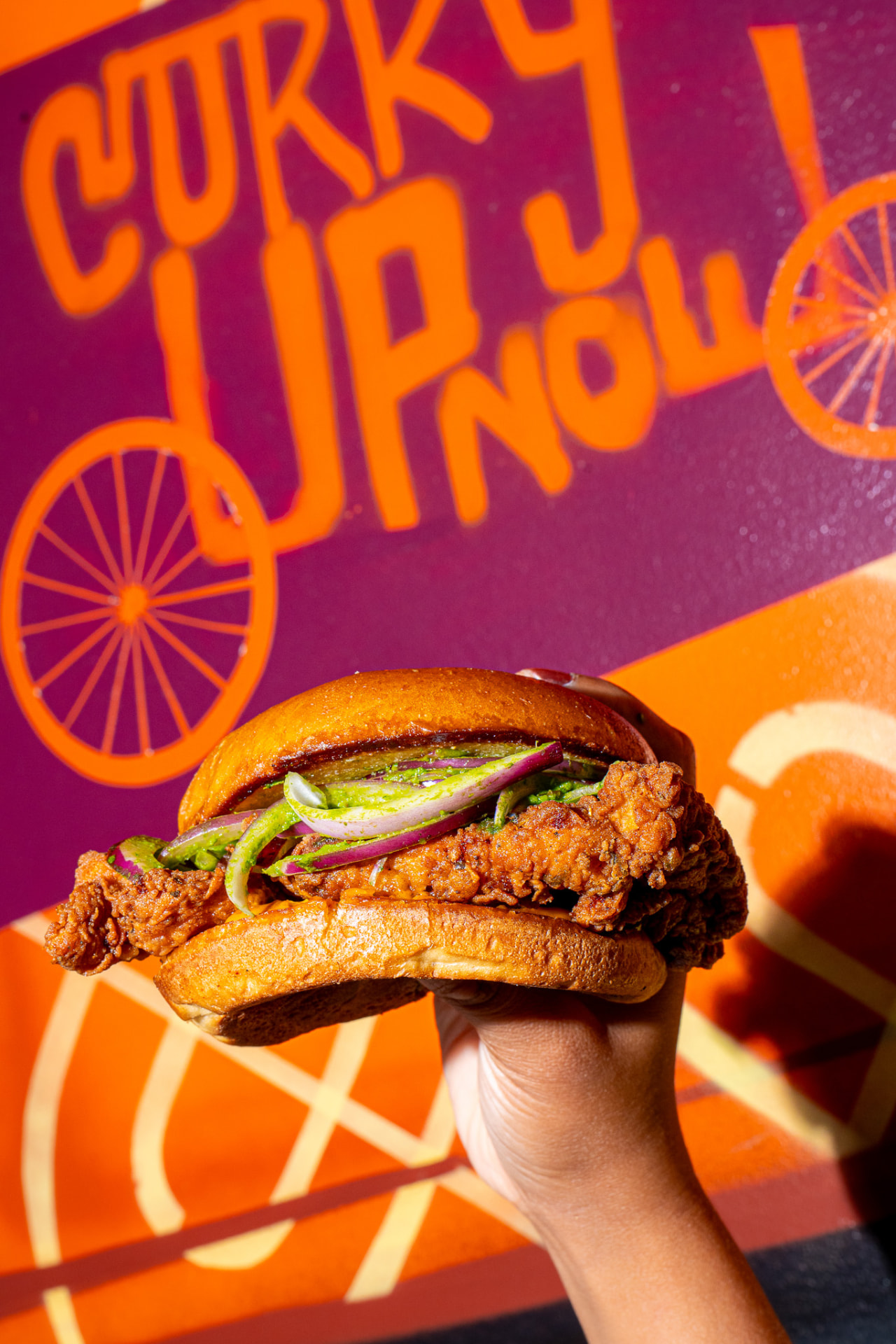 Tandoori chicken sandwich held up against the mural