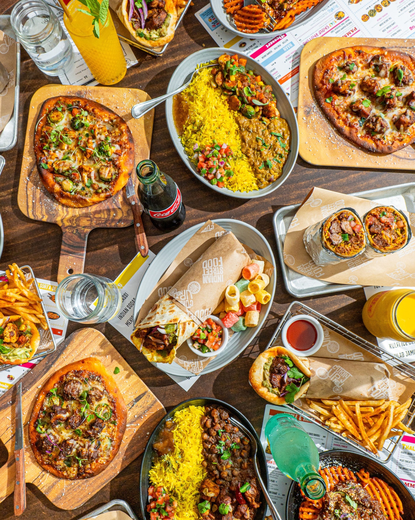 Full table spread: naughty naans, bowls, burritos, kathi roll, fries and drinks
