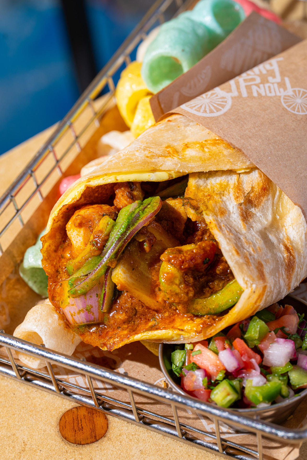 Kathi roll with fryums and pico, wrapped in branded paper, side angle